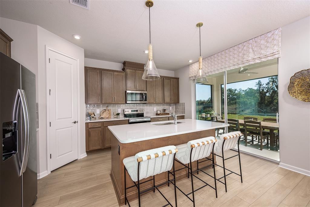 A modern kitchen features wood cabinets, a white quartz island, and a sliding glass door — 1758 SOARING VIDA STREET, PALMETTO, FL