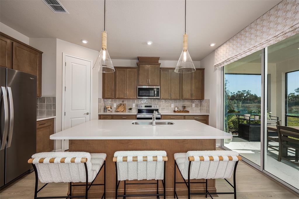 A kitchen with wood cabinets, a white island, stainless steel appliances, and a sliding glass door — 1758 SOARING VIDA STREET, PALMETTO, FL
