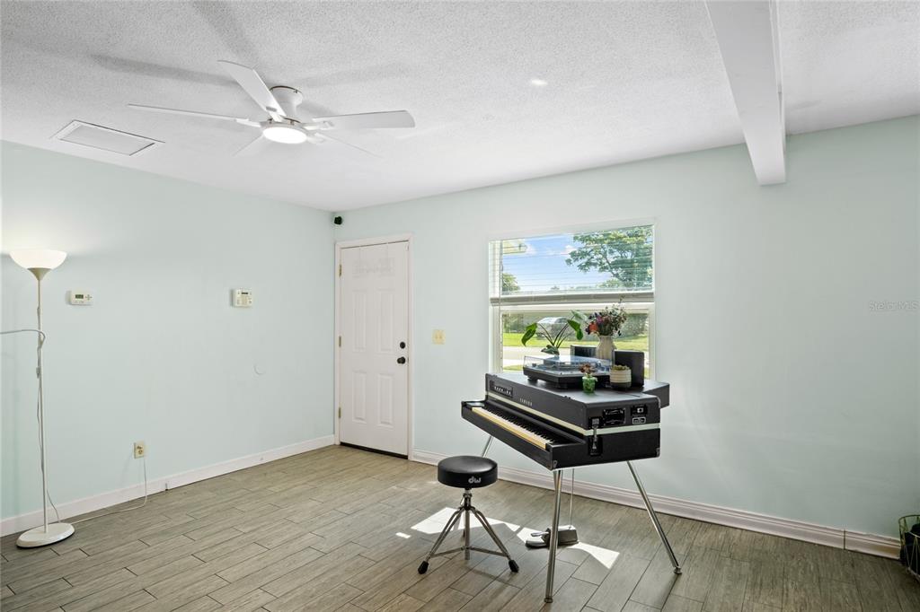 A living room features a piano, a tall bookshelf, and a dark blue accent wall — 7924 PLUNKETT AVENUE, ORLANDO, FL