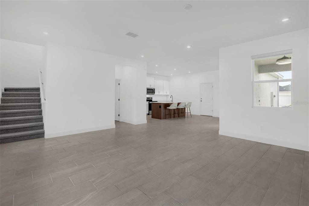 An open-concept living area features gray tile flooring, a staircase, and a kitchen with an island — 9544 ARCHWAY ALLEY, ORLANDO, FL