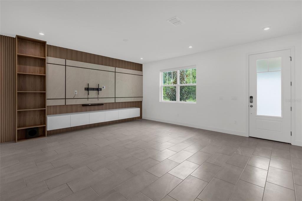 A living room features a large media wall with wood slats, built-in shelving, and tile flooring — 9544 ARCHWAY ALLEY, ORLANDO, FL