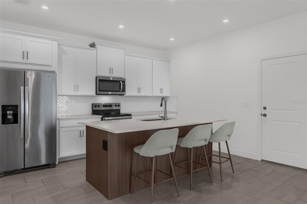 A modern kitchen features white cabinetry, stainless steel appliances, a dark wood island, and bar stools — 9544 ARCHWAY ALLEY, ORLANDO, FL
