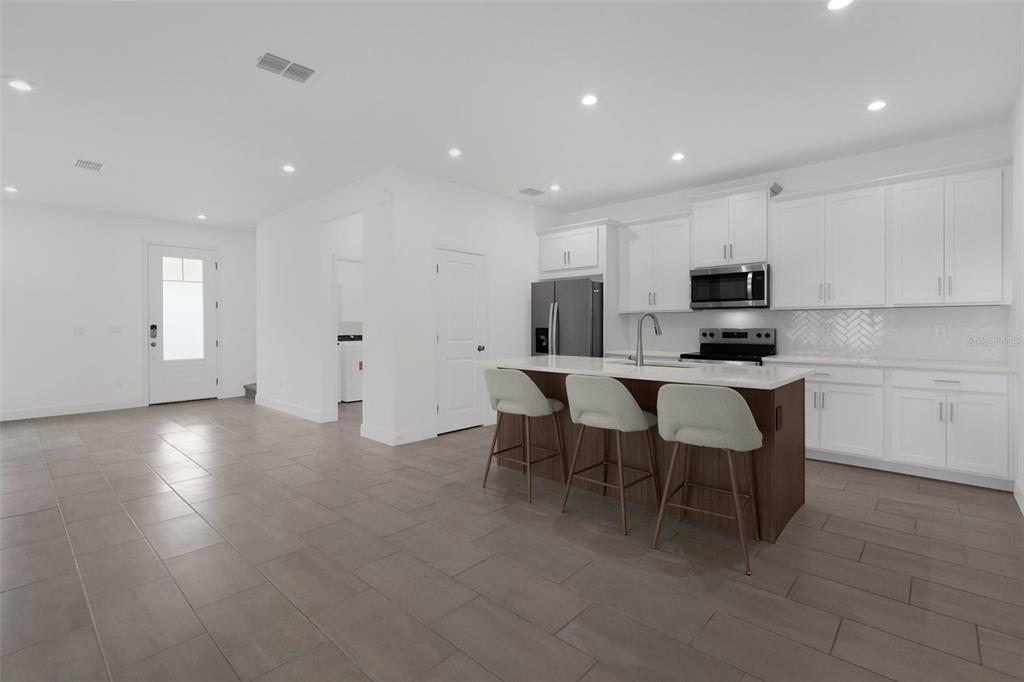 A modern kitchen features white cabinetry, a dark wood island with bar stools, and tile flooring — 9544 ARCHWAY ALLEY, ORLANDO, FL