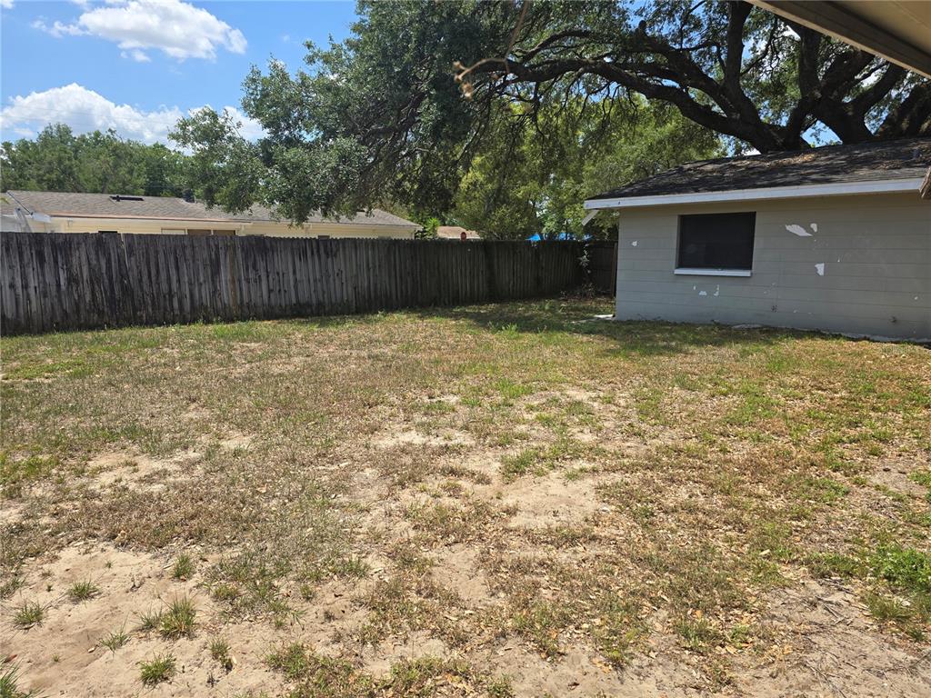 A backyard with a sandy lawn, a wooden fence, and a small detached building — 6124 11TH STREET, ZEPHYRHILLS, FL