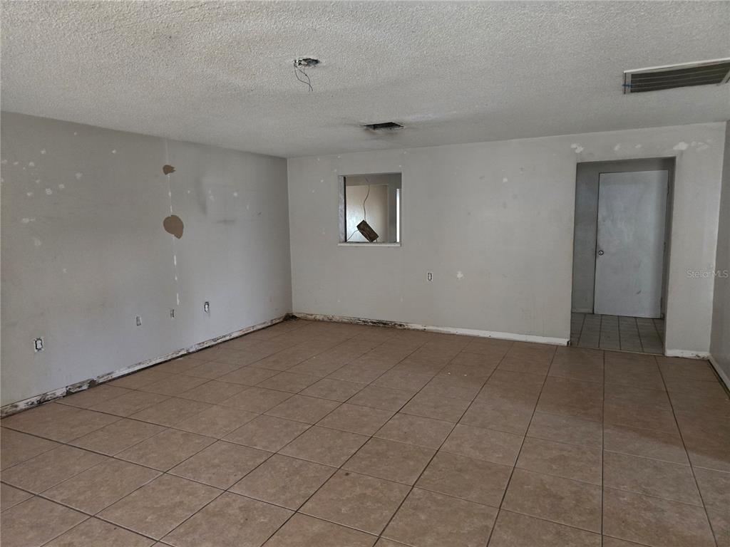 An empty room with beige tile flooring, unfinished drywall, and a pass-through window — 6124 11TH STREET, ZEPHYRHILLS, FL