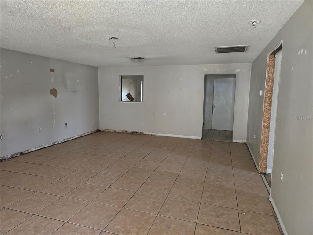 An unfinished room with beige floor tiles, gray walls, and exposed ceiling wiring — 6124 11TH STREET, ZEPHYRHILLS, FL