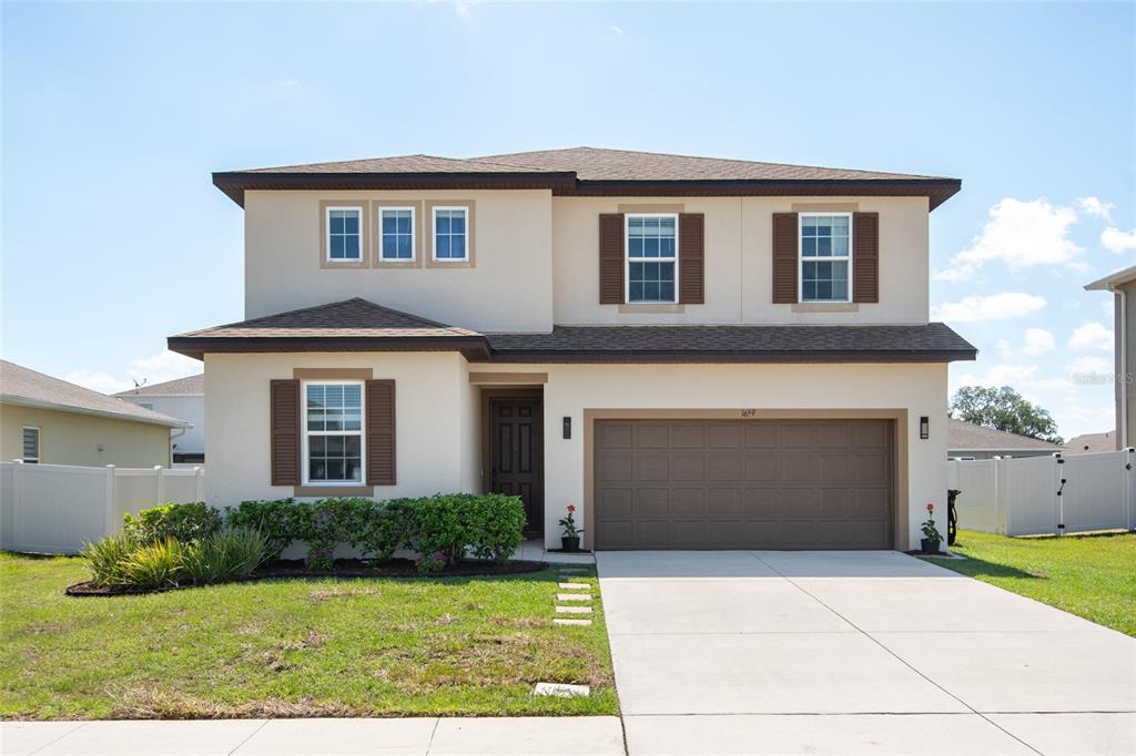 A two-story suburban house with a beige stucco exterior, brown shutters, and a two-car garage — 1659 GENTLE BREEZE DRIVE, ST CLOUD, FL