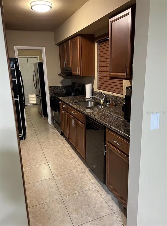 A galley kitchen features dark wood cabinets, granite countertops, and black appliances — 660 CARL BOLTER DRIVE, DELRAY BEACH, FL