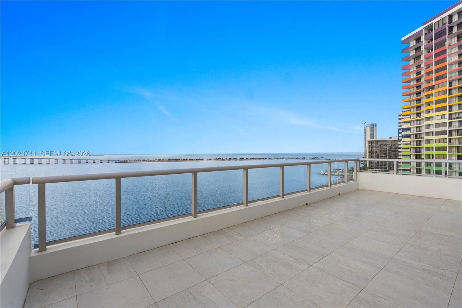 A spacious balcony with light-colored tile flooring overlooks a large body of water — 1541 Brickell Ave # C1607, Miami FL 33129, MIAMI, FL