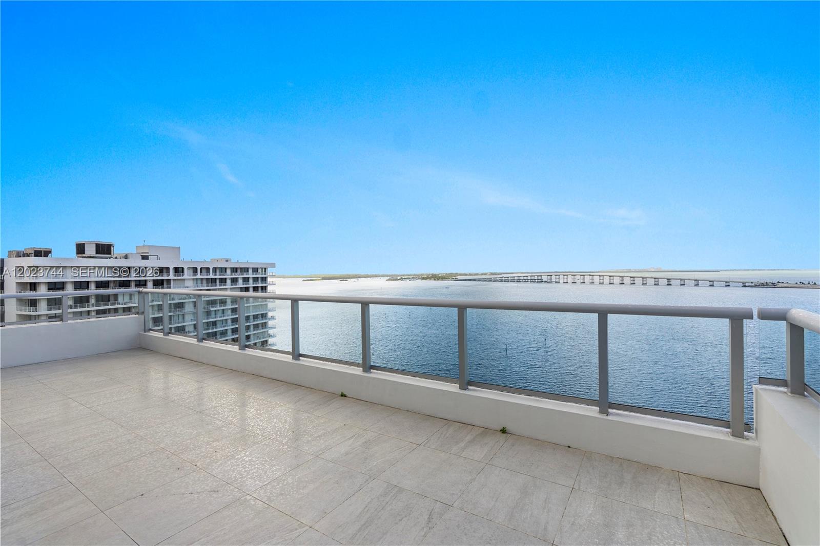 A balcony with light-colored tile flooring overlooks a large body of water and a bridge — 1541 Brickell Ave # C1607, Miami FL 33129, MIAMI, FL