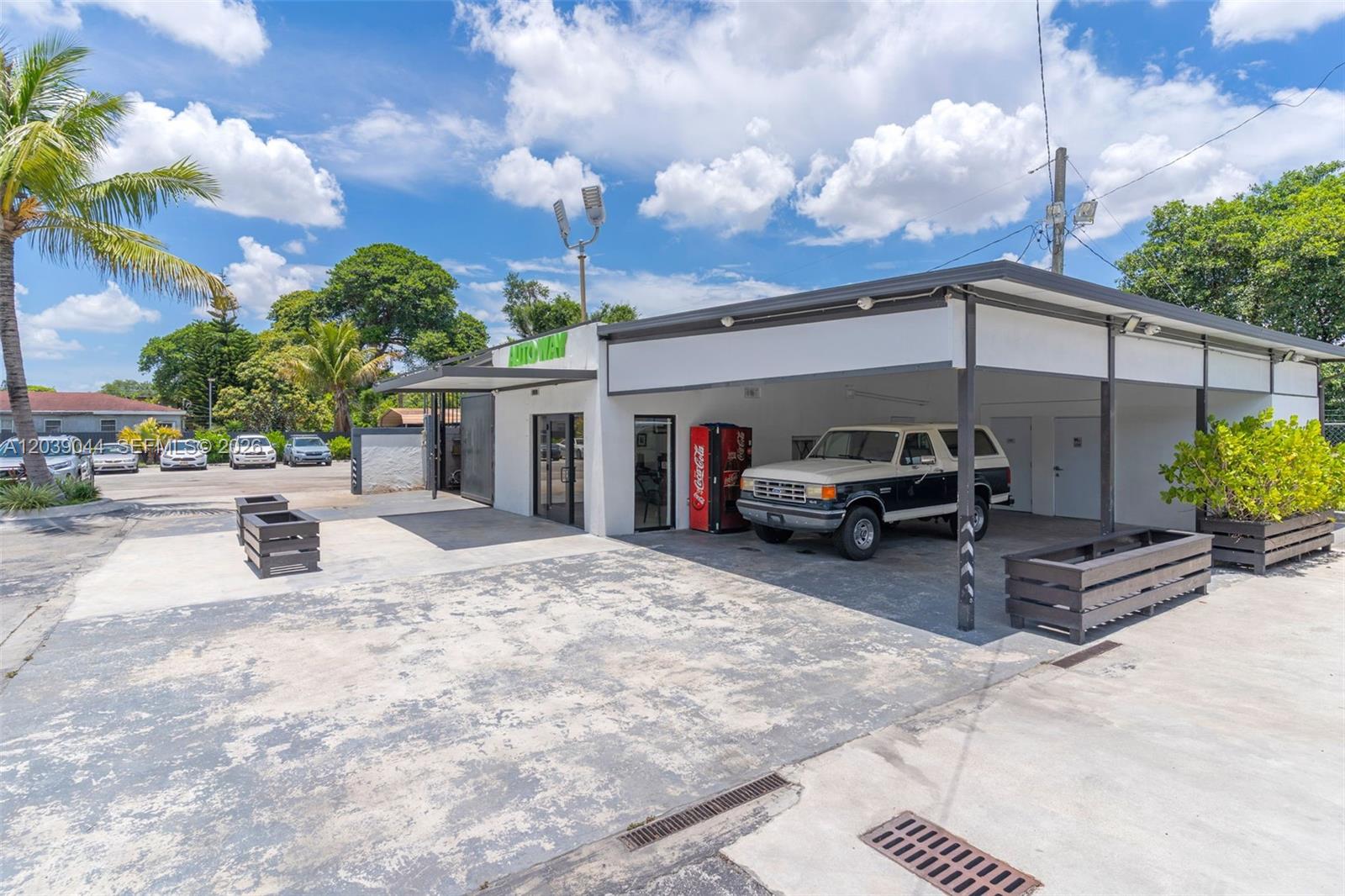 An exterior view of a commercial building with a covered parking area and a truck — 2729 NW 56th St, Miami FL 33142, MIAMI, FL