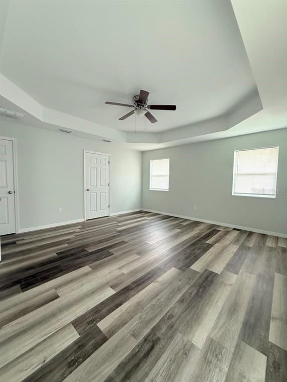 A bedroom features a tray ceiling, a ceiling fan, two windows, and wood-look flooring — 6823 SW 129TH STREET, OCALA, FL