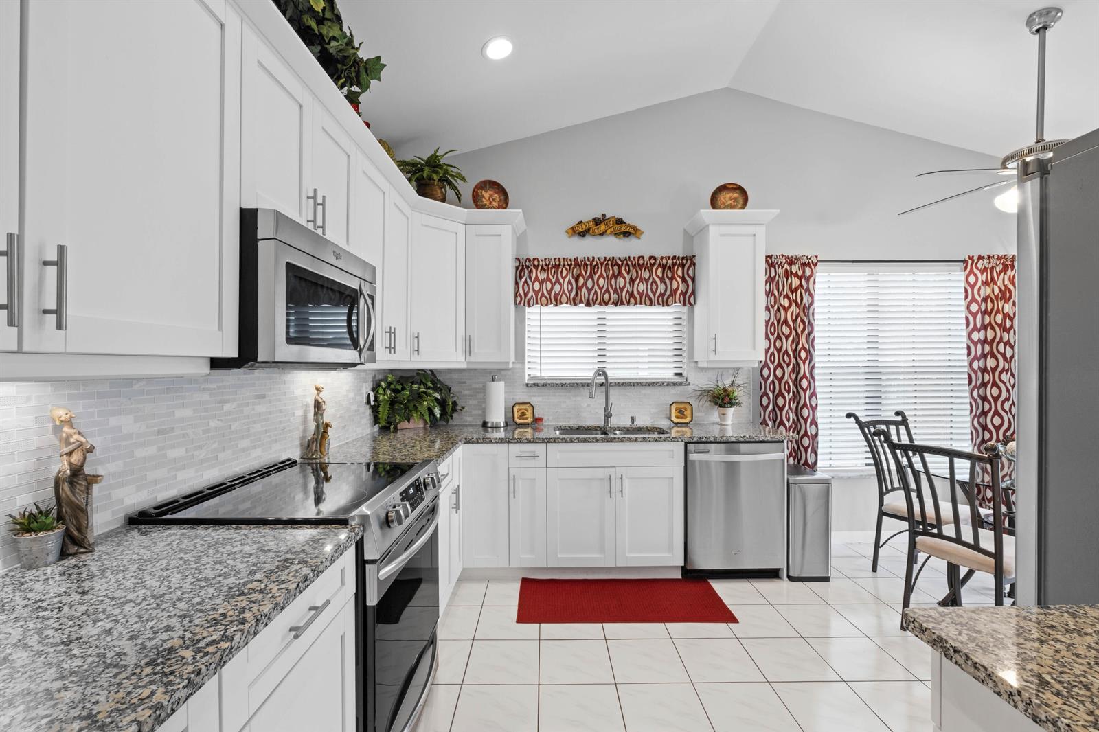 A kitchen features white cabinets, granite countertops, stainless steel appliances, and white tile flooring — 3327 Jog Park Drive # 4022, FL 33467, FL