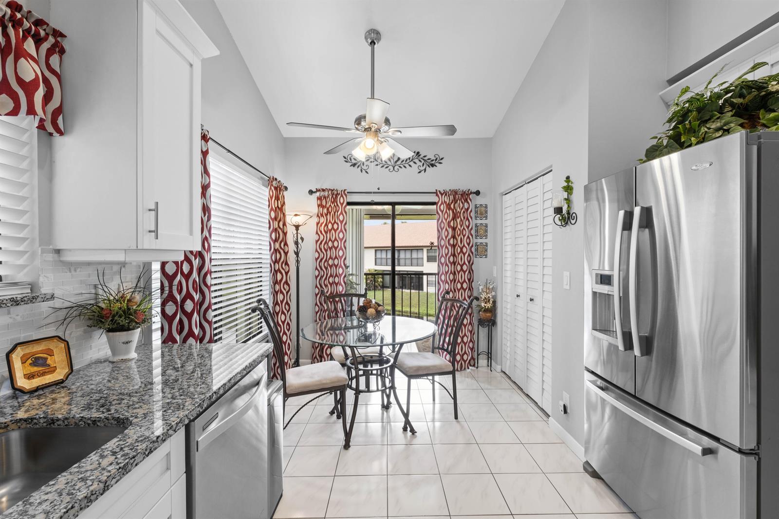 A kitchen breakfast nook features a glass table, stainless steel appliances, and red patterned curtains — 3327 Jog Park Drive # 4022, FL 33467, FL