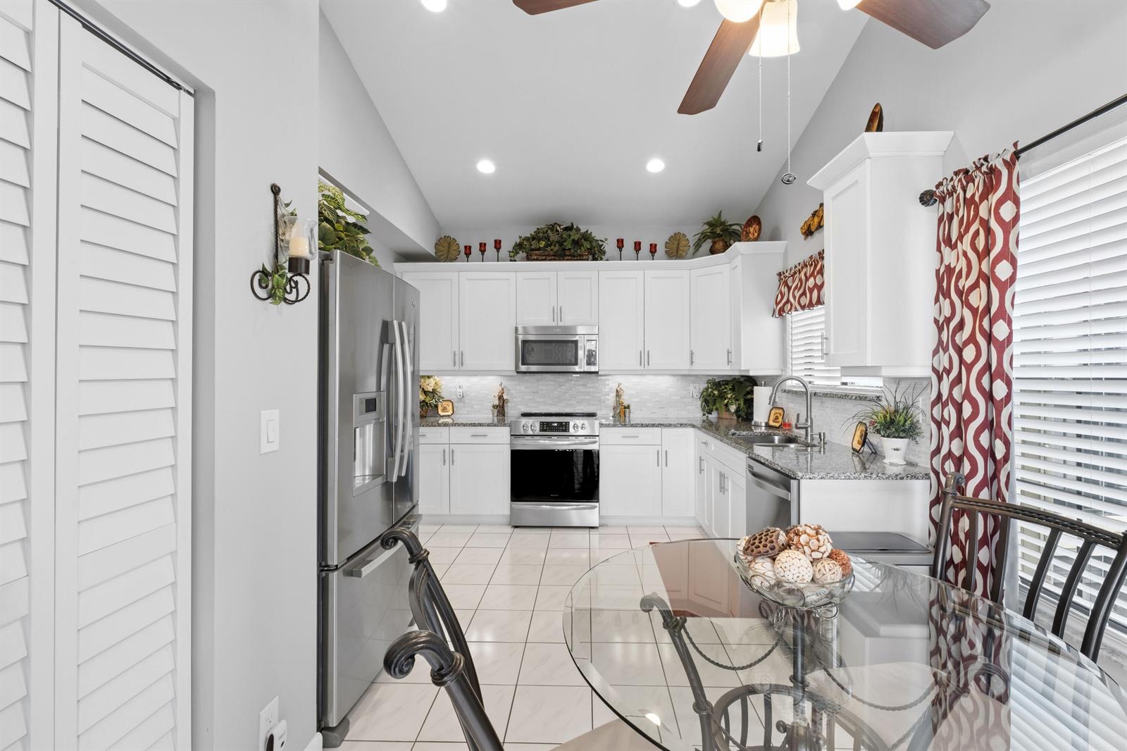 A kitchen features white cabinetry, stainless steel appliances, granite countertops, and a glass dining table — 3327 Jog Park Drive # 4022, FL 33467, FL