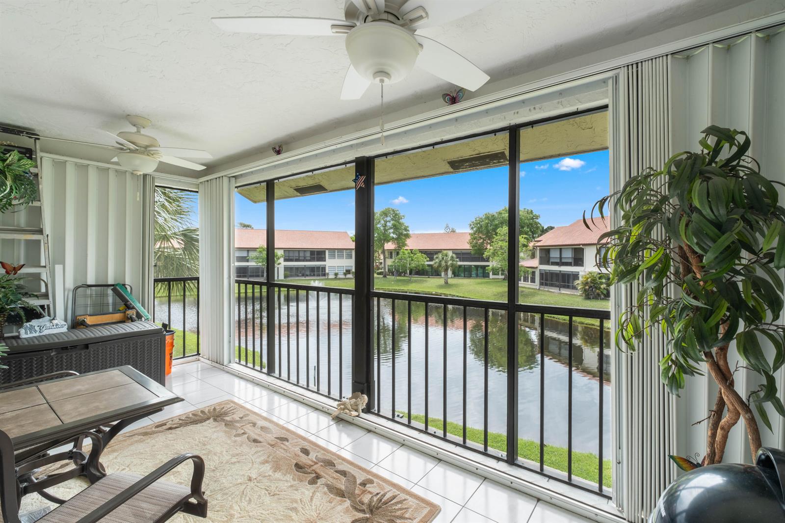 A screened-in balcony with tile flooring overlooks a lake and neighboring apartment buildings — 3327 Jog Park Drive # 4022, FL 33467, FL