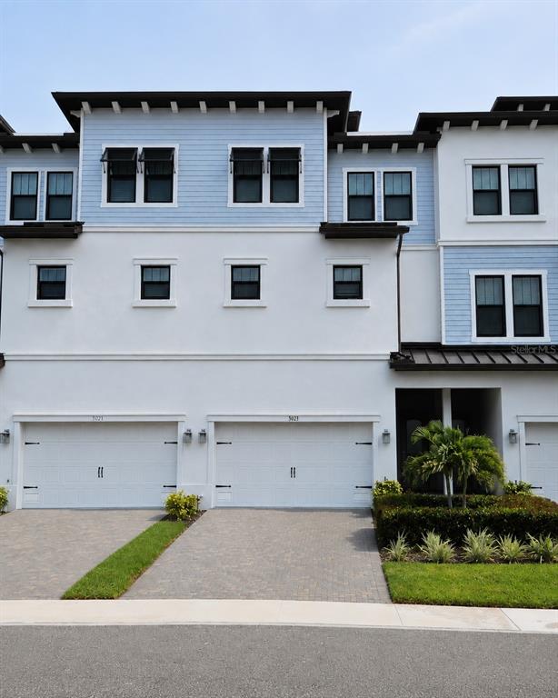 The exterior of a multi-story townhouse features white stucco, blue siding, and two garage doors — 3023 BERMUDA SLOOP CIRCLE, RUSKIN, FL