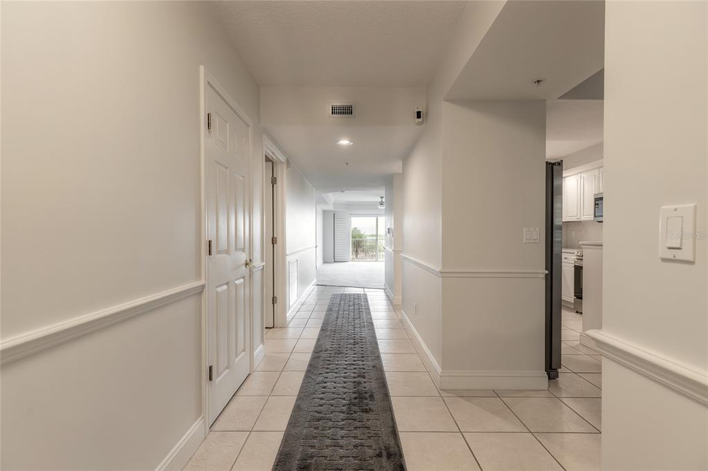 A tiled hallway with a long runner rug leads toward a bright living area — 4650 LINKS VILLAGE DRIVE UNIT A401, PONCE INLET, FL
