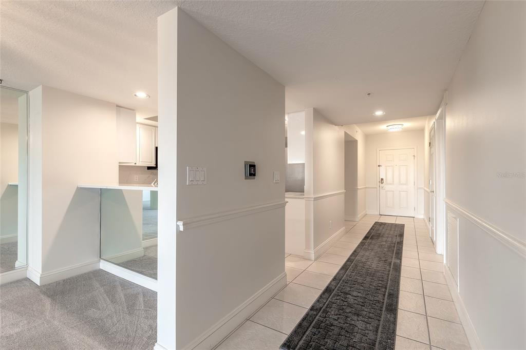 A hallway with white walls and tile flooring leads to a white front door — 4650 LINKS VILLAGE DRIVE UNIT A401, PONCE INLET, FL