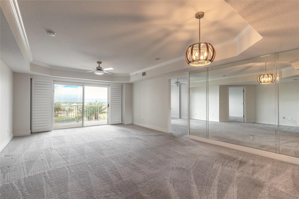 A spacious carpeted bedroom features a tray ceiling, mirrored wall, and sliding doors to a balcony — 4650 LINKS VILLAGE DRIVE UNIT A401, PONCE INLET, FL