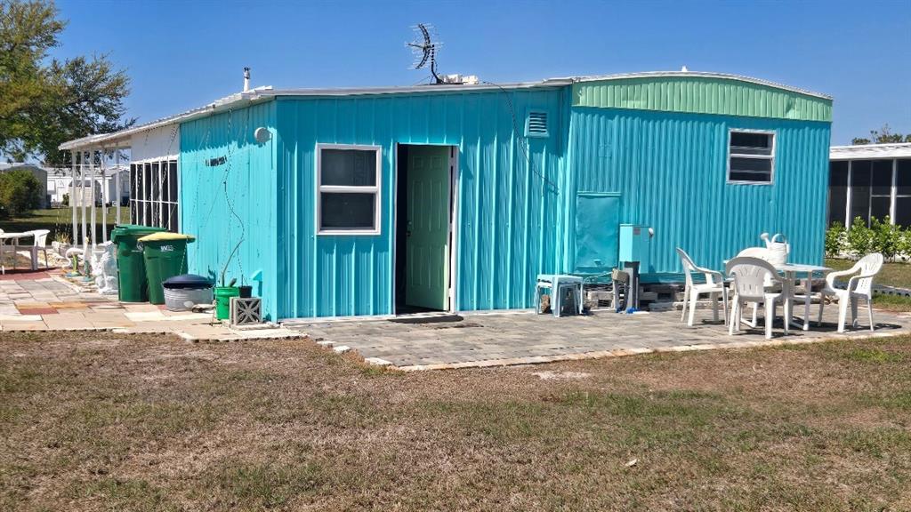 A bright blue mobile home features a paved patio area with outdoor furniture and trash cans — 1393 MALLARD DRIVE, ENGLEWOOD, FL