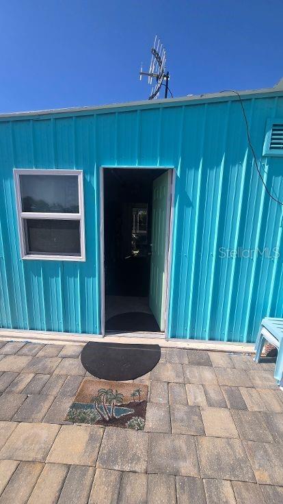 A bright blue metal-sided building features an open doorway and a window above a patio — 1393 MALLARD DRIVE, ENGLEWOOD, FL