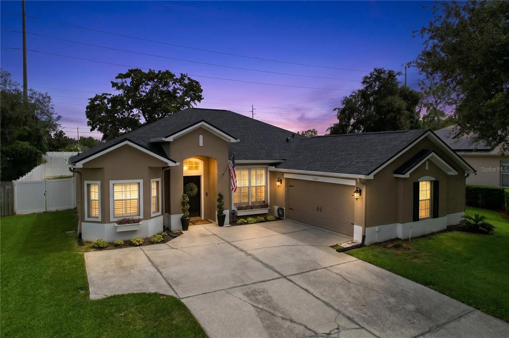 A tan single-story house with a two-car garage and a concrete driveway at dusk — 1748 BROOKSTONE WAY, PLANT CITY, FL