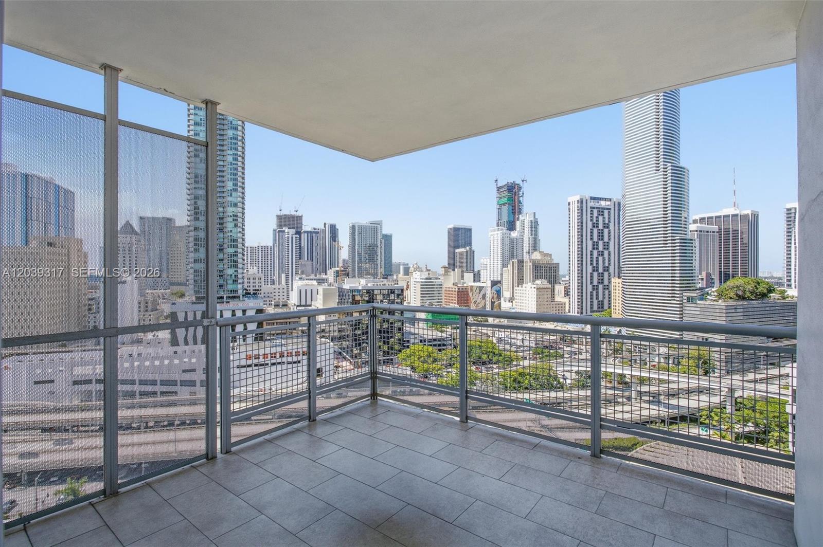 A balcony with tiled flooring and metal railings overlooks a dense urban skyline — 350 S Miami Ave # 1903, Miami FL 33130, MIAMI, FL