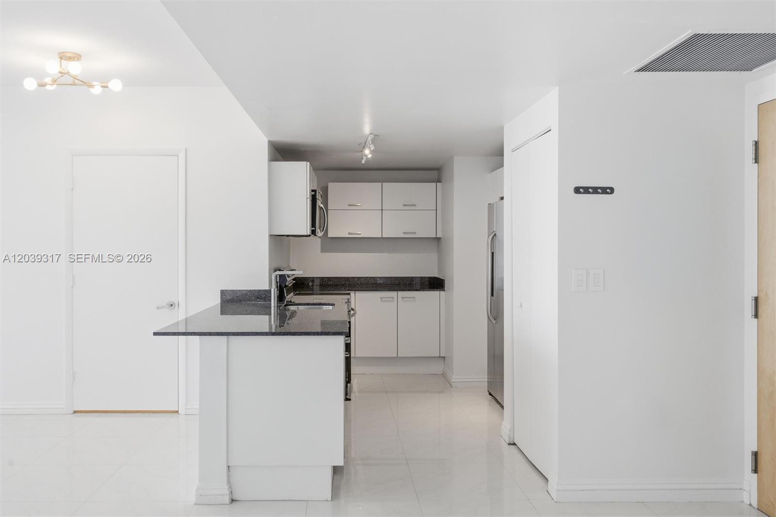 A kitchen features white cabinets, dark granite countertops, stainless steel appliances, and white tile flooring — 350 S Miami Ave # 1903, Miami FL 33130, MIAMI, FL