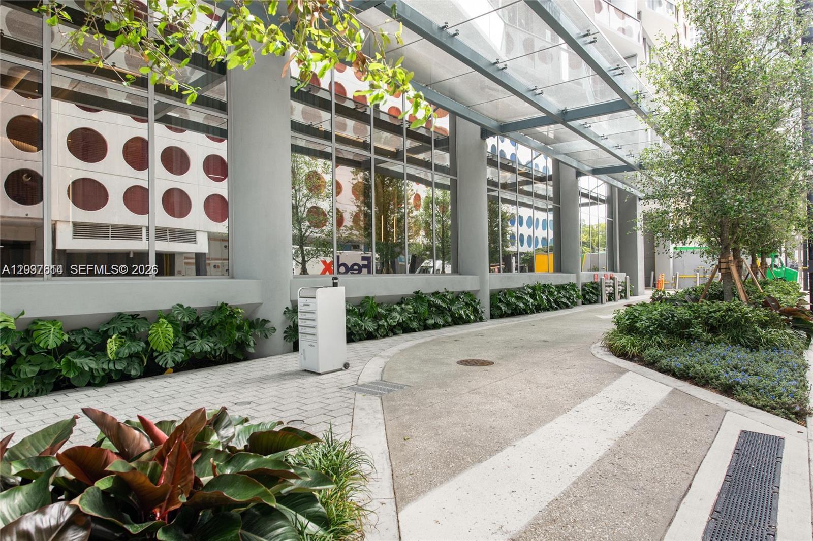 A paved walkway leads past a modern building exterior with large windows and glass awnings — 77 SE 5th Street # 2914, Miami FL 33131, MIAMI, FL