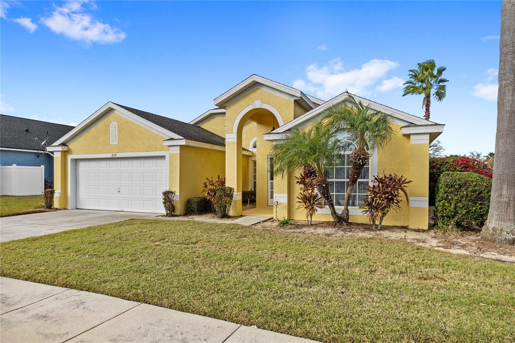 A yellow single-story house with a two-car garage, arched entryway, and palm tree landscaping — 235 BALLYSHANNON DRIVE, DAVENPORT, FL