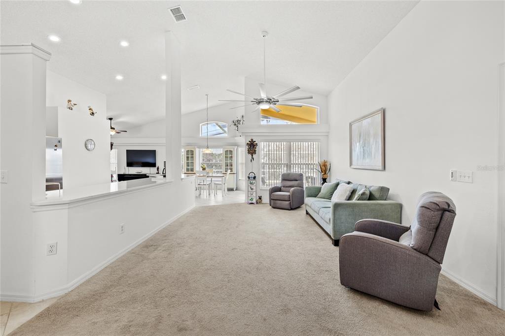 A living room with carpeted floors, a sofa, two armchairs, and an open kitchen view — 235 BALLYSHANNON DRIVE, DAVENPORT, FL