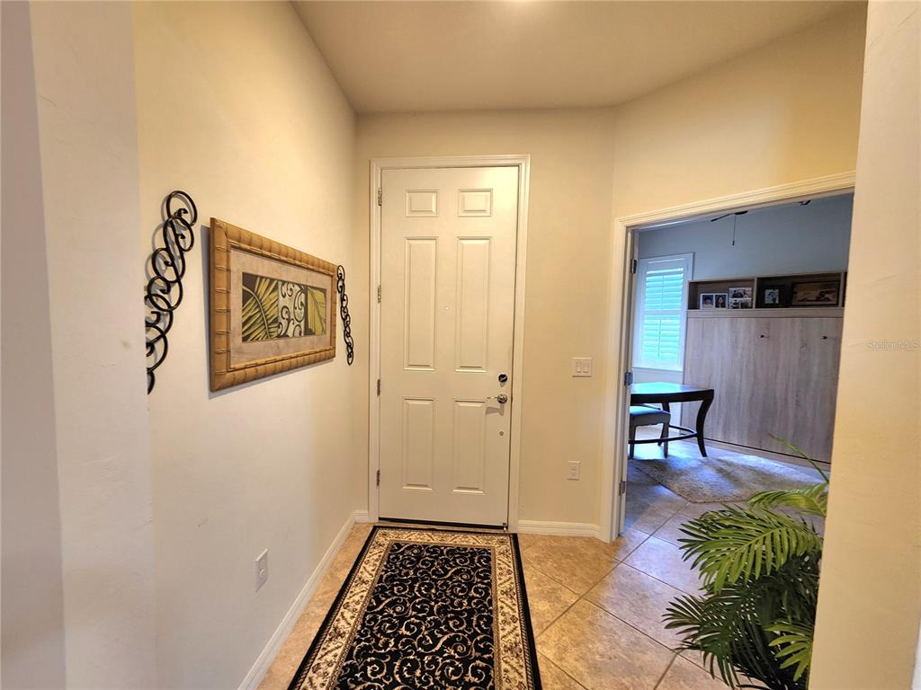 An entryway features a white door, tiled flooring, a decorative wall hanging, and an adjacent room — 13892 ALAFAYA STREET, VENICE, FL