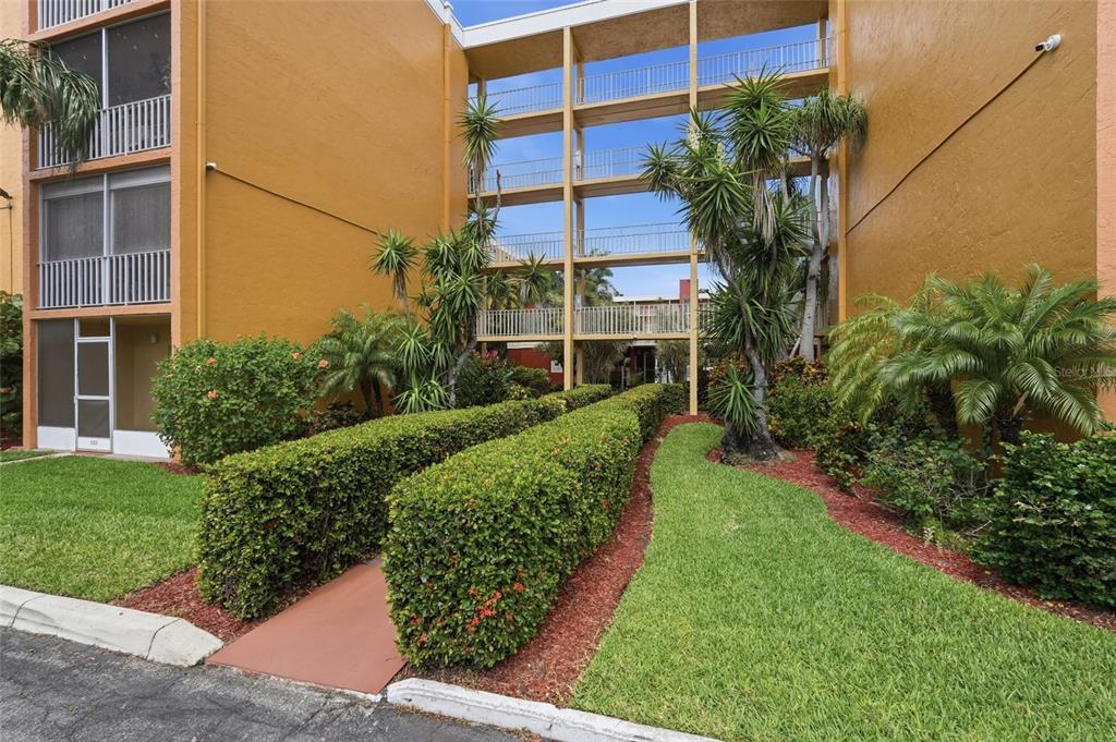 An exterior view of a multi-story apartment building with a landscaped walkway and hedges — 2366 E MALL DRIVE UNIT 403, FORT MYERS, FL