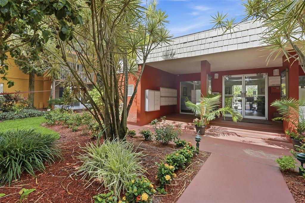 The exterior entrance of a residential building features a red facade, glass doors, and landscaping — 2366 E MALL DRIVE UNIT 403, FORT MYERS, FL
