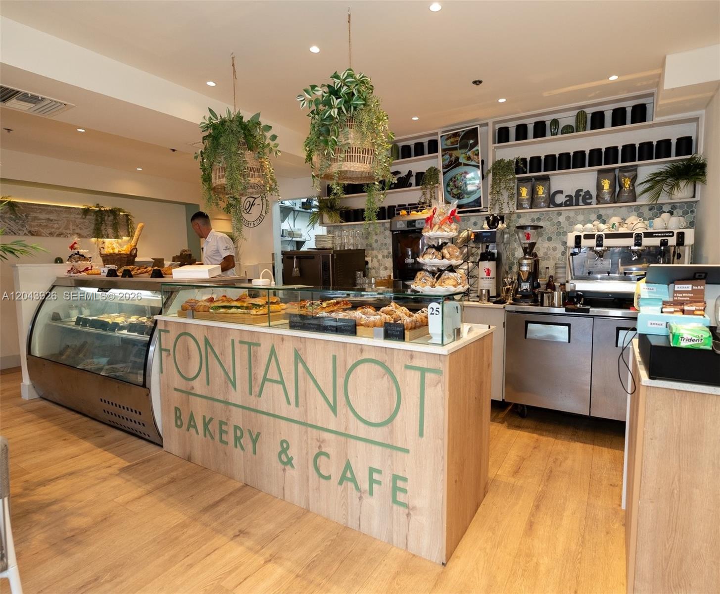 A bakery and cafe interior features a wooden service counter, display cases, and hanging plants — 1300 Collins NE St, Miami FL 33139, MIAMI, FL