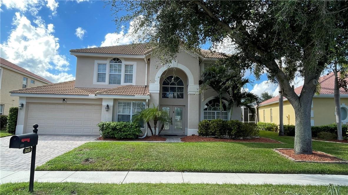 A two-story beige house with a tiled roof, arched entryway, and a paved driveway — 3620 Hamilton Key, West Palm Beach FL 33411, WEST PALM BEACH, FL