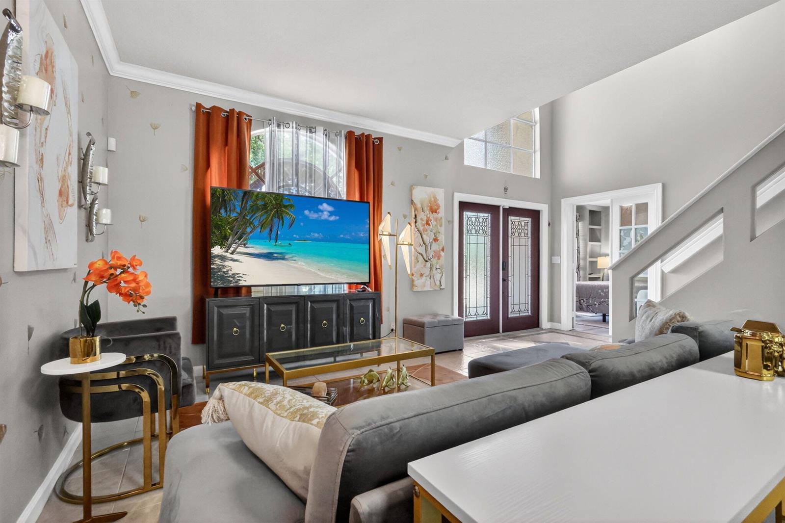 A living room features a large television, gray sofa, and double front doors — 3620 Hamilton Key, West Palm Beach FL 33411, WEST PALM BEACH, FL