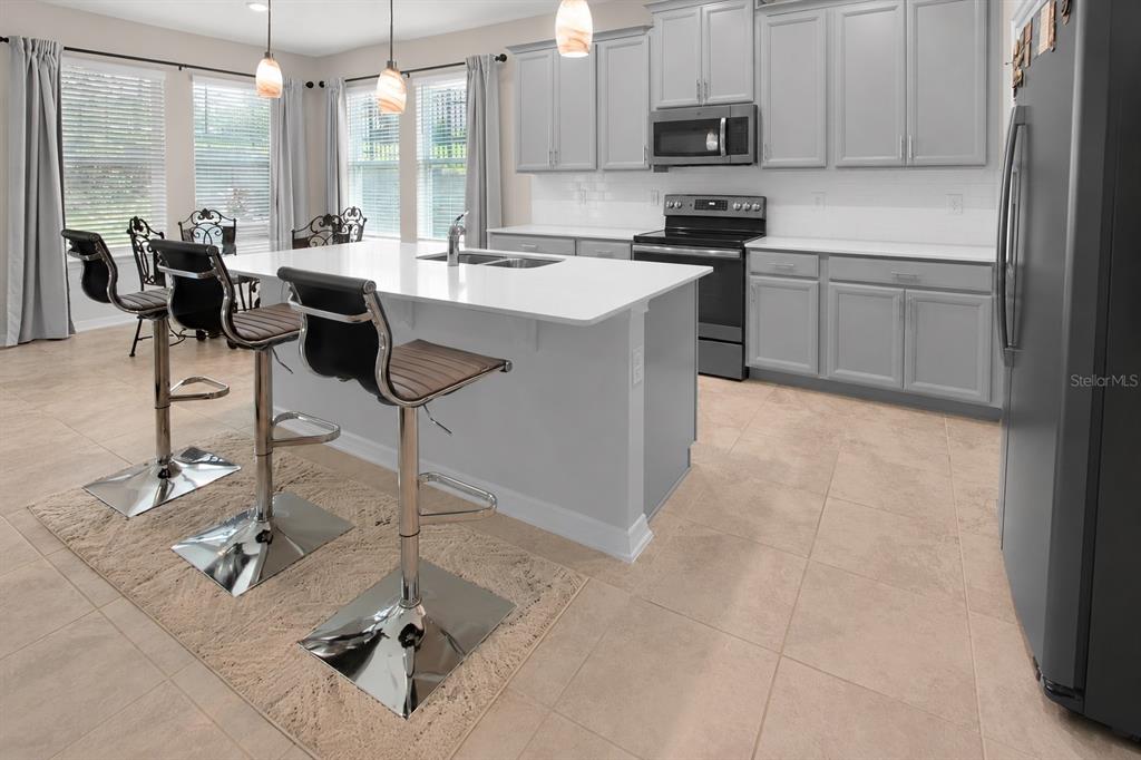 A kitchen with a white island, gray cabinets, stainless steel appliances, and tile flooring — 987 WAX MYRTLE AVENUE, MINNEOLA, FL