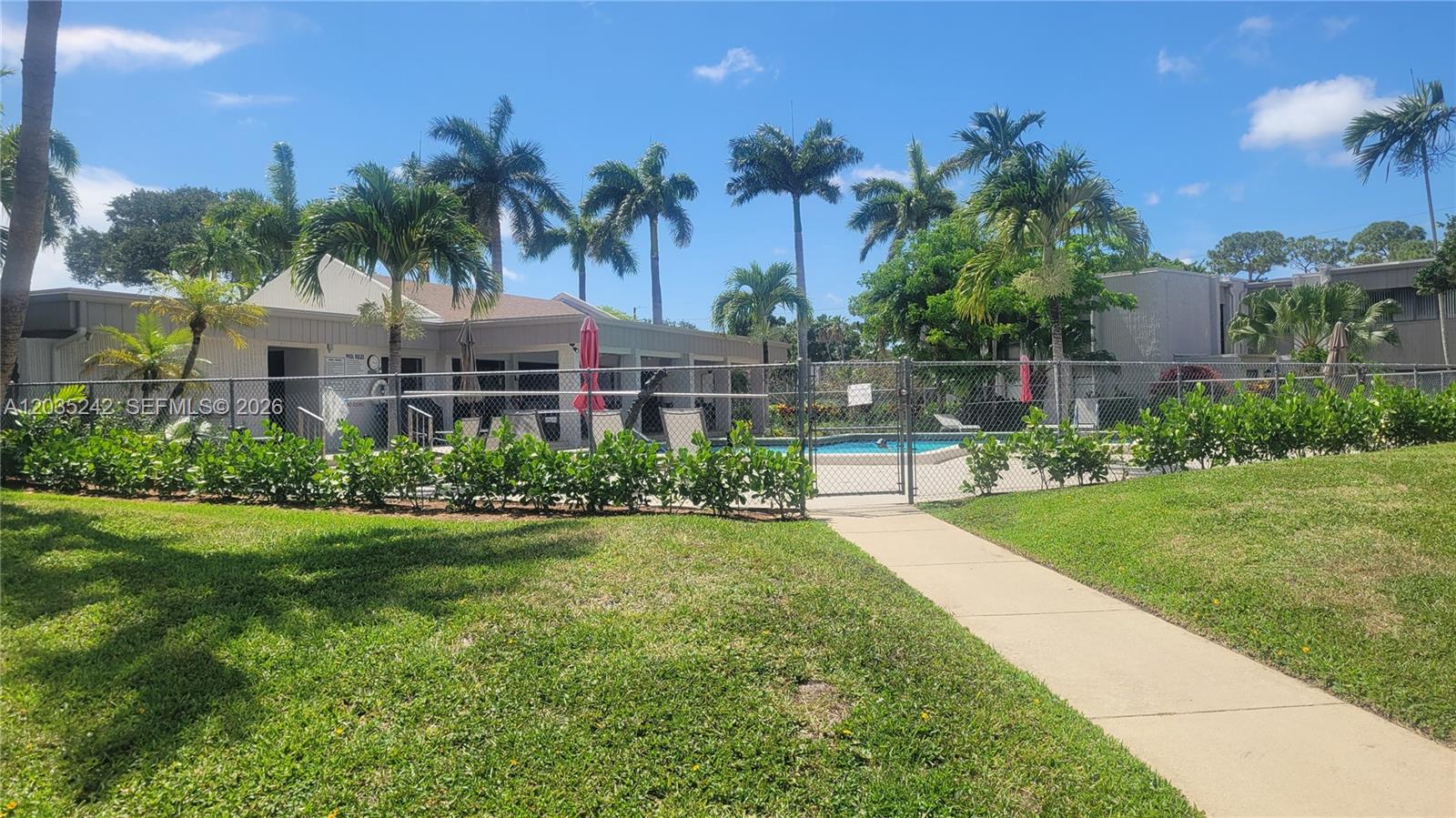 A fenced swimming pool area is surrounded by palm trees and a grassy lawn — 6666 Spring Bottom Way # 179, Boca Raton FL 33433, BOCA RATON, FL