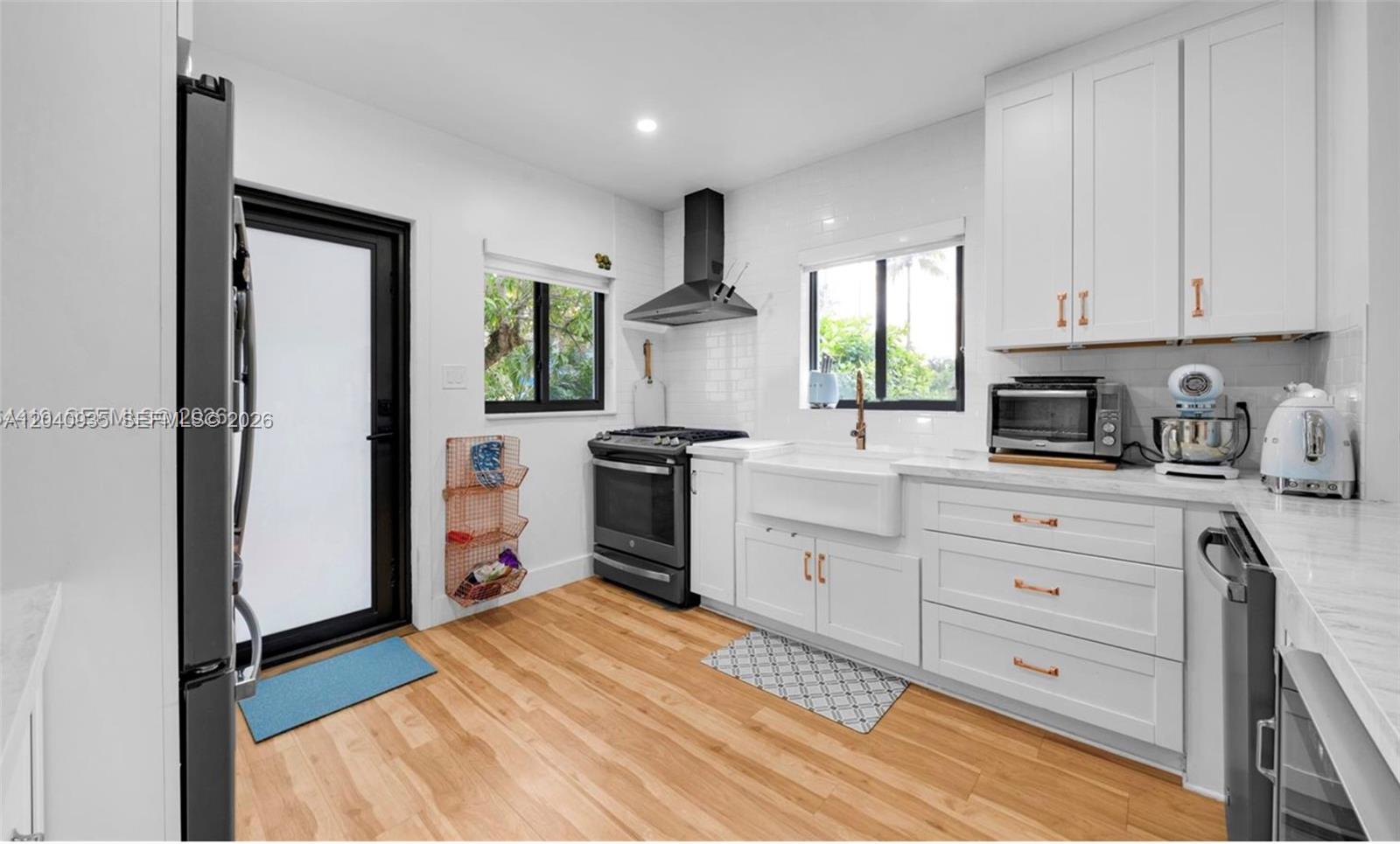 A bright kitchen features white cabinets, a farmhouse sink, stainless steel appliances, and wood flooring — 375 SW 32nd Rd, Miami FL 33129, MIAMI, FL