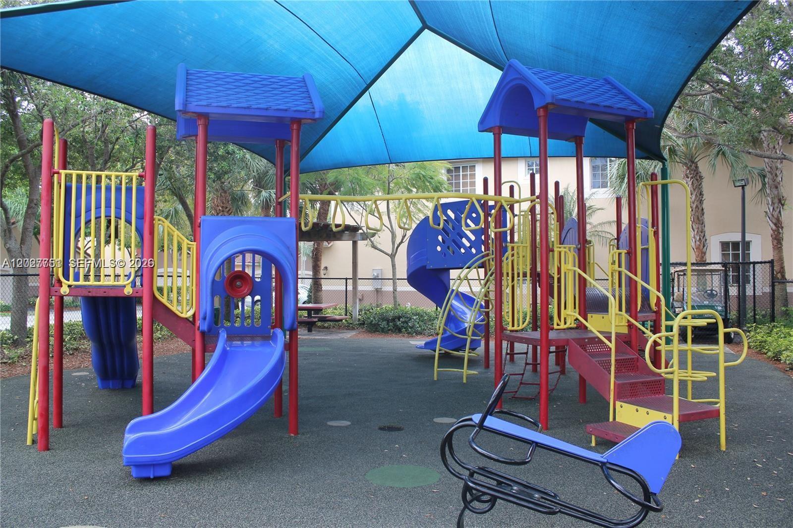 A colorful outdoor playground features multiple slides, climbing structures, and a large blue shade canopy — 3677 San Simeon Cir # 3677, Weston FL 33331, WESTON, FL