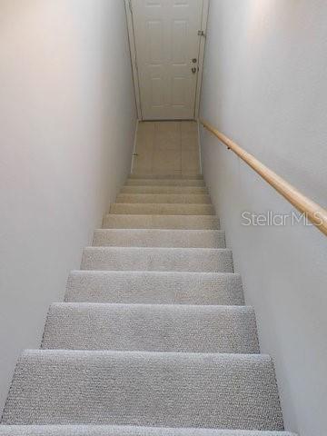 A carpeted staircase leads down to a closed white door with a wooden handrail — 1669 MONARCH DRIVE UNIT 204, VENICE, FL