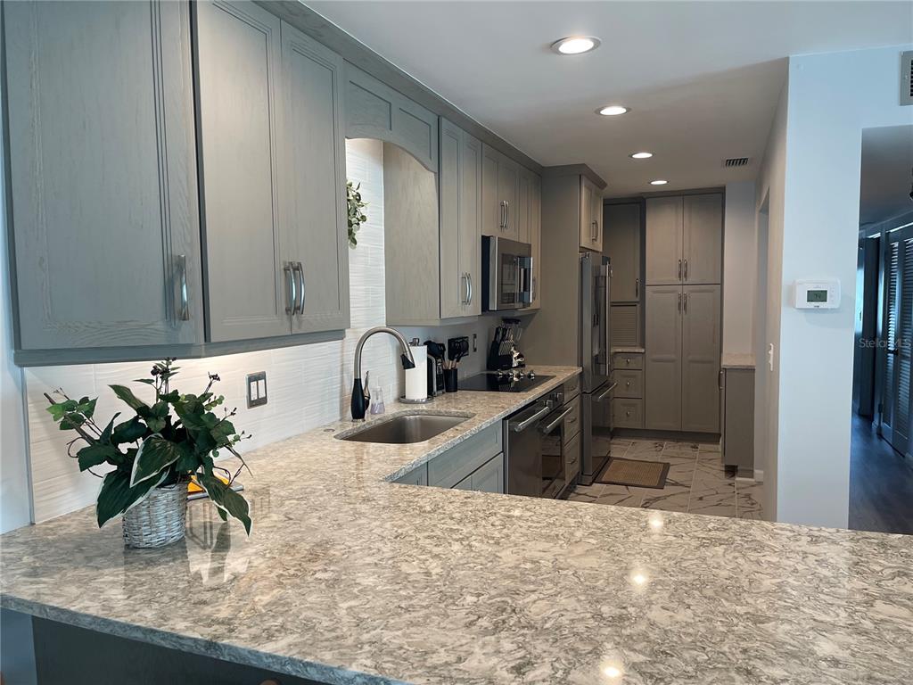 A kitchen features gray cabinets, granite countertops, stainless steel appliances, and a white tiled backsplash — 5400 GULF DRIVE UNIT 32, BRADENTON BEACH, FL