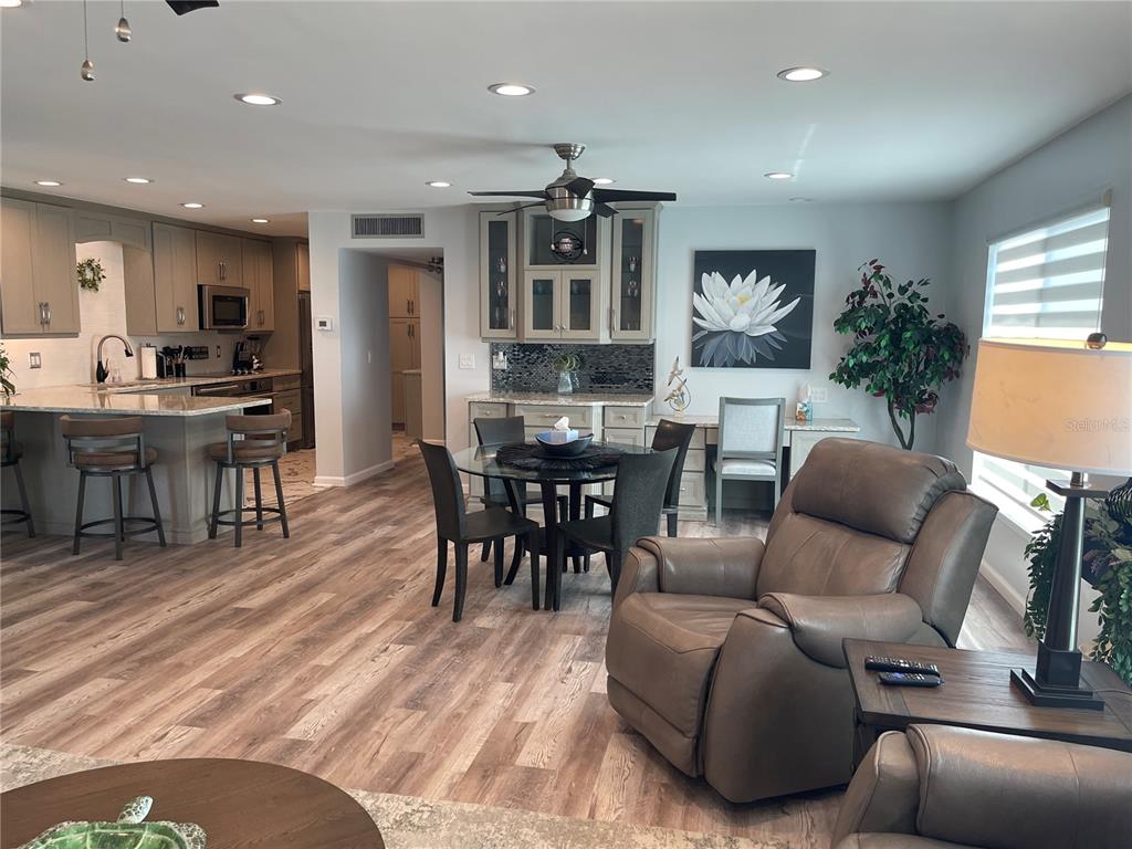 An open-concept kitchen and dining area features wood-look flooring, grey cabinetry, and a leather recliner — 5400 GULF DRIVE UNIT 32, BRADENTON BEACH, FL