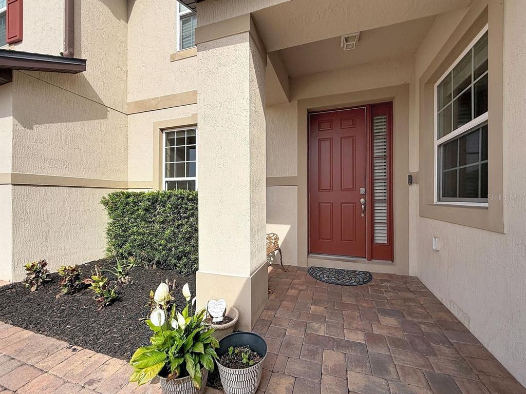 A red front door with a side window sits under a covered porch with pavers — 2771 WESTYN COVE LANE, OCOEE, FL