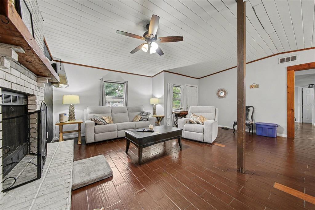 A living room features a white brick fireplace, wood-plank ceiling, and dark wood flooring — 231 E 1ST STREET, CHULUOTA, FL