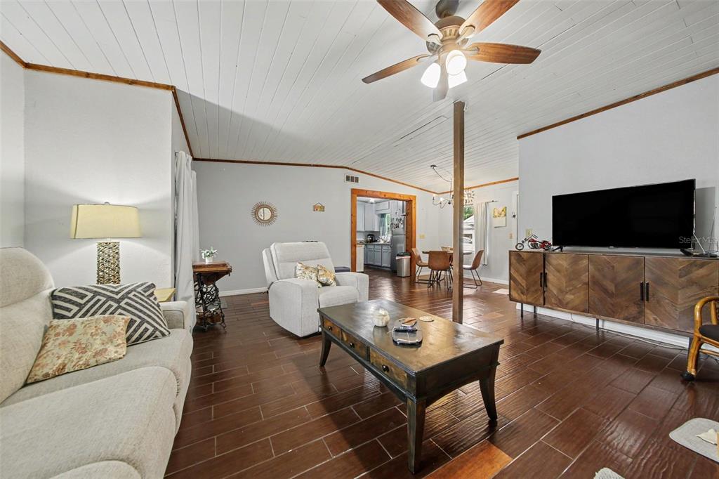 A living room features dark wood-look tile floors, white plank ceilings, and an open layout — 231 E 1ST STREET, CHULUOTA, FL