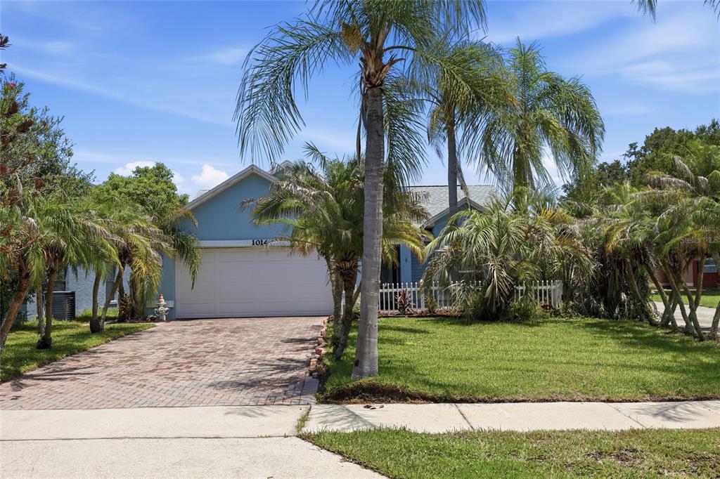 A blue single-story house with a brick driveway, palm trees, and a white garage door — 1014 CONLEY DRIVE, OVIEDO, FL