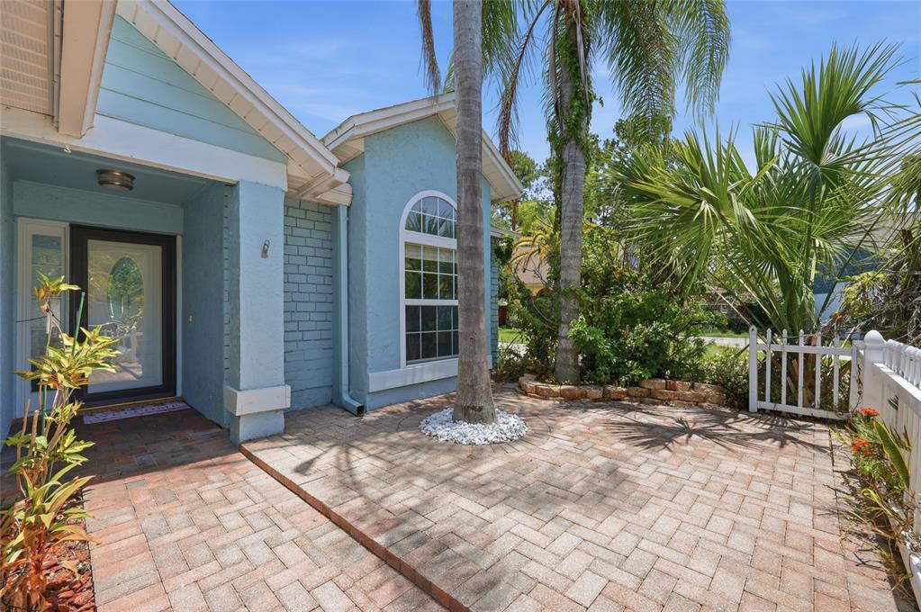 A light blue house exterior features a brick-paved patio, a palm tree, and a white fence — 1014 CONLEY DRIVE, OVIEDO, FL